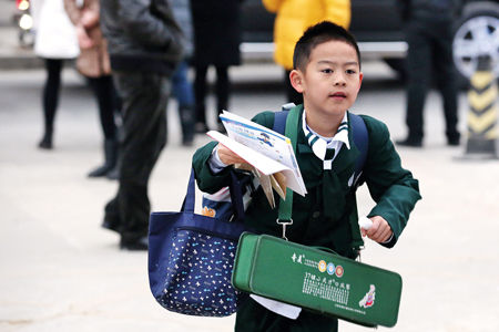 小学生背着书包拿着书进入学校。这是2013年，北京17.5万人报名“幼升小”挤进小学。