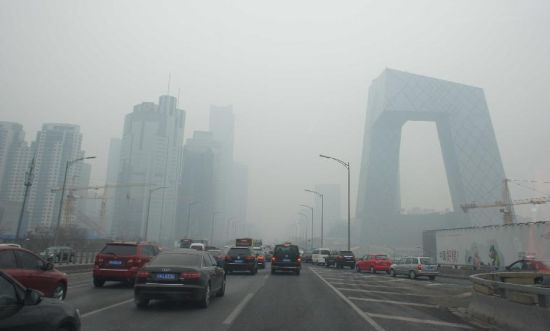 　　2月21日，车辆行驶在雾霾笼罩的北京街头，中央电视台新址大楼依稀可见。 
