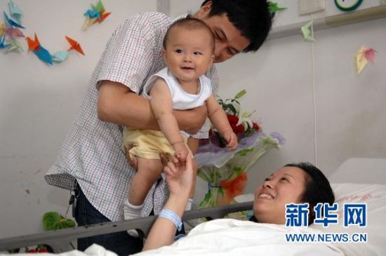 资料图：7月11日，丈夫陈建国将7个月大的儿子陈至轩抱至病床边，吴菊萍开心地牵着儿子的手。新华社记者黄宗治 摄