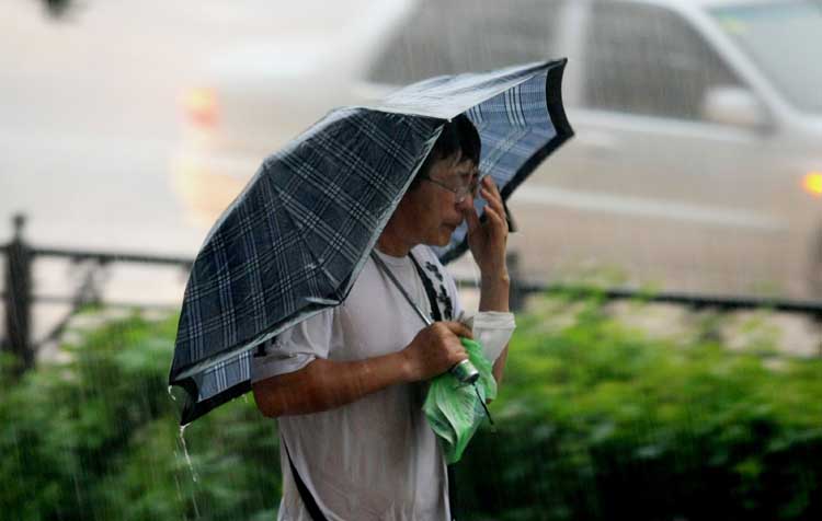 图文:撑伞行人边擦脸上雨水边向前走