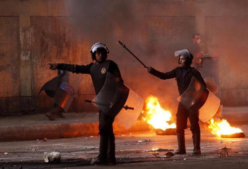 两名埃及警察站在被示威者点燃的汽车轮胎前面。