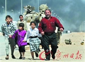 2003年3月28日，在伊拉克南部城市巴士拉的英军阵地上，一家伊拉克难民经过一辆被炮弹摧毁的伊拉克T-55坦克。（资料图片）