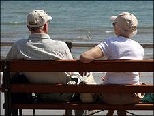 An elderly couple sitting on a bench by the sea