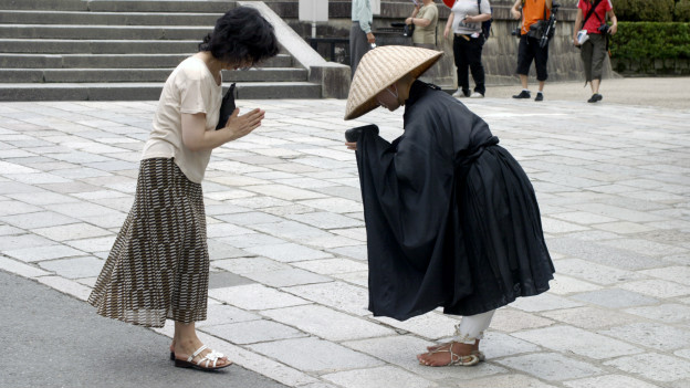 A Japanese woman bows in greeting to a monk.