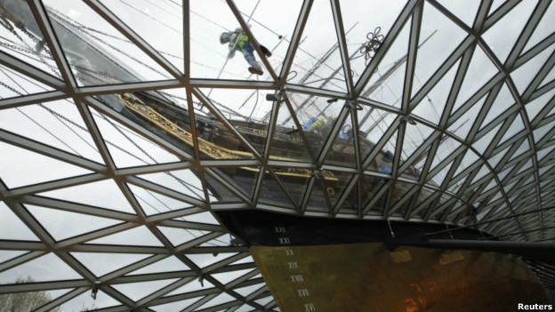 A worker cleans new windows around the old tea clipper ship, Cutty Sark.