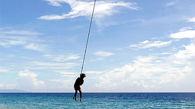 A girl swings on a rope attached to a palm tree on Bonegi beach.