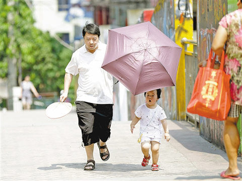 重庆九龙坡区黄桷坪正街,一位父亲打着遮阳伞拿着蒲扇护送孩子出行.