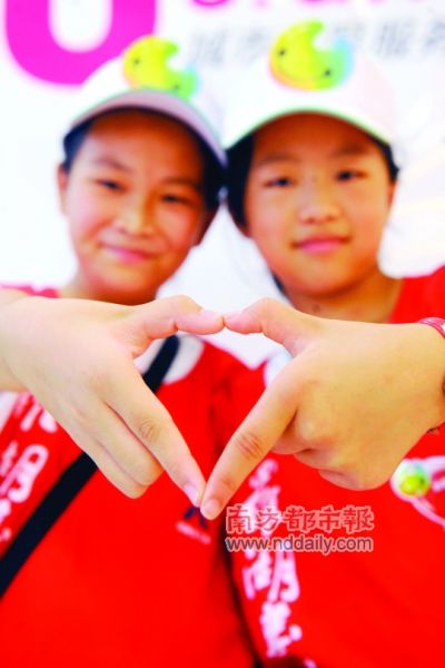 两位小志愿者在u站前做着爱心手势,体验大运志愿者的工作.